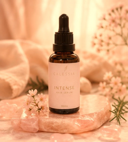 Calessia Intense Hair Serum bottle on a rose quartz slab with cherry blossom and rosemary